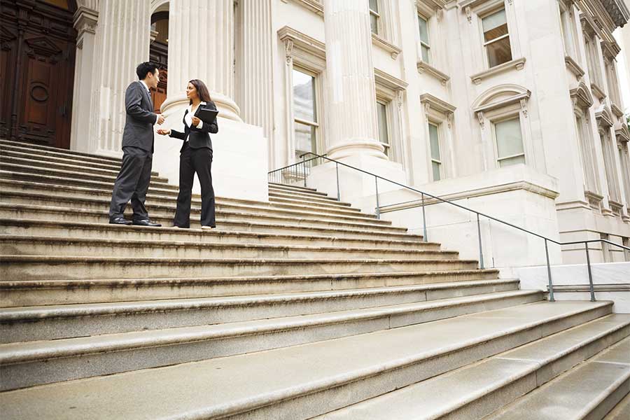 Two attorneys talking to each other on the steps outside of a courthouse